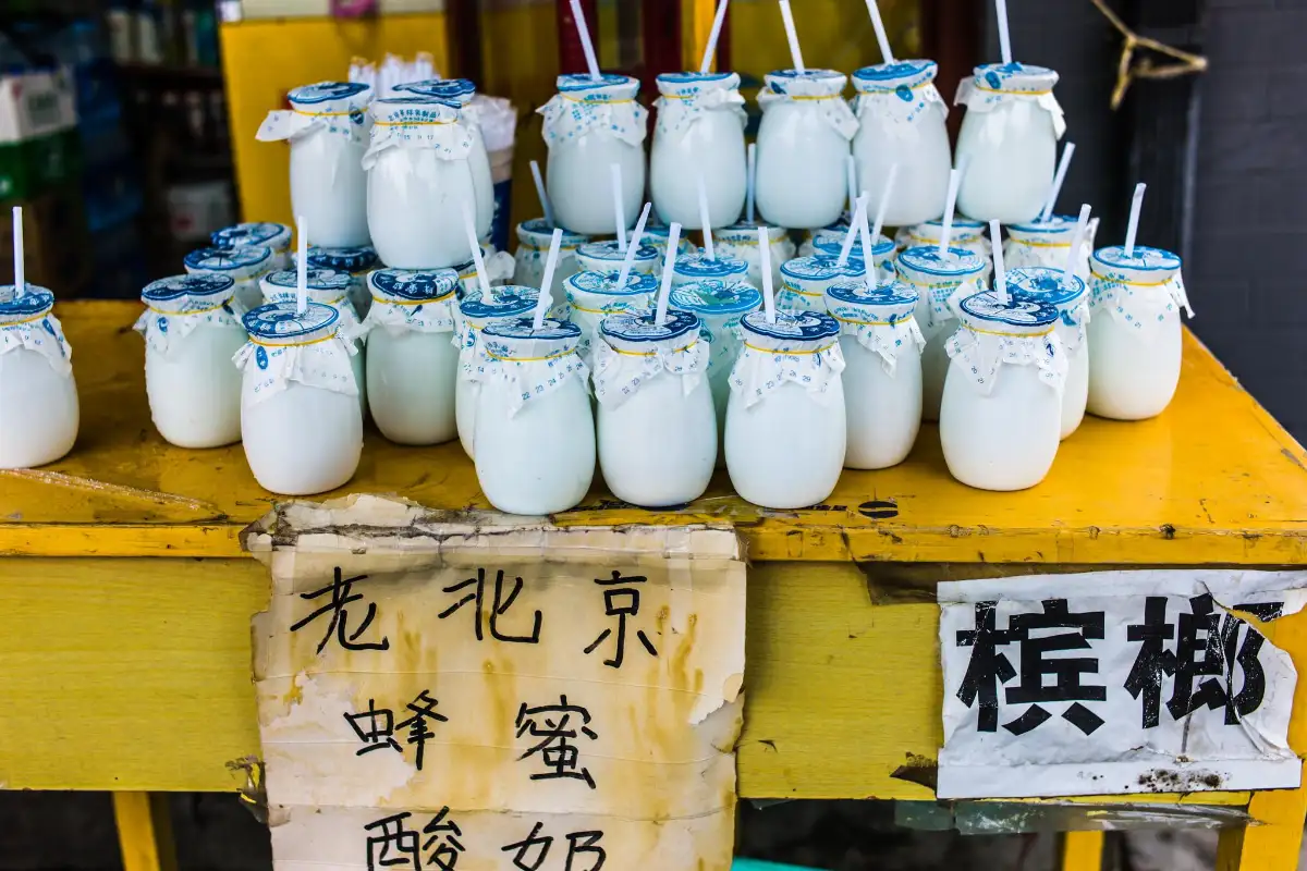 Old Beijing Honey Yogurt street stall with glass jars, blue lids, and straws on yellow table