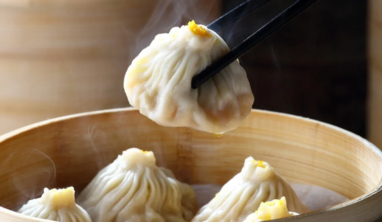 Fresh steamed buns held with chopsticks over bamboo steamer with more buns inside
