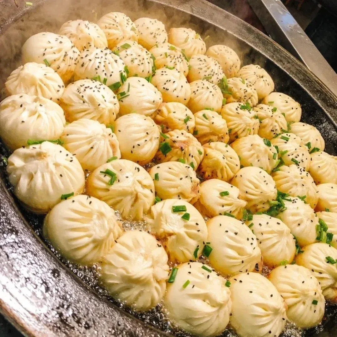 Freshly cooked steamed buns in a pan with black sesame seeds and chopped green onions topping