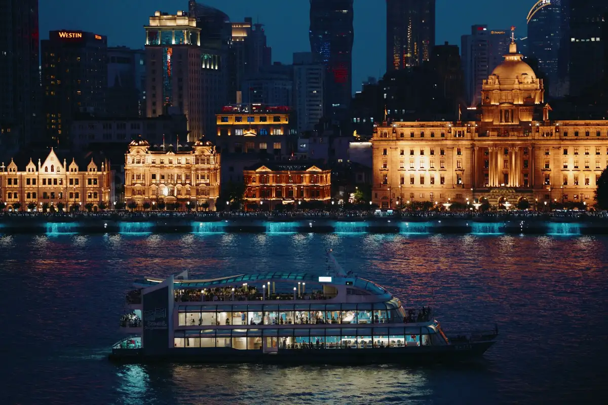 Nighttime cityscape with illuminated cruise ship on river, historic European architecture and modern skyscrapers in background
