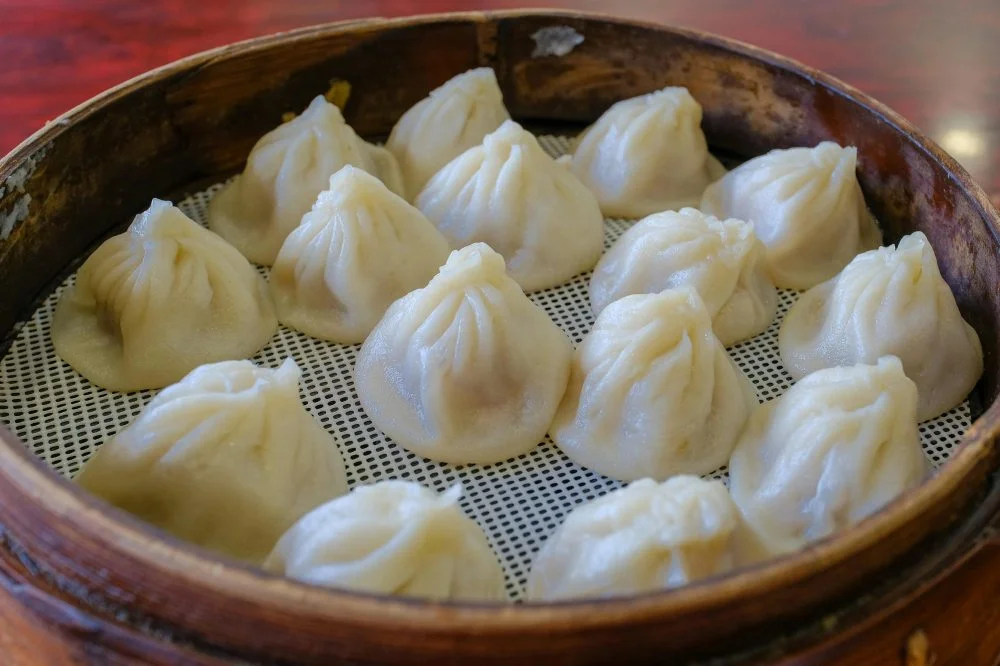 Freshly steamed fluffy buns in traditional bamboo steamer basket, Chinese dim sum breakfast