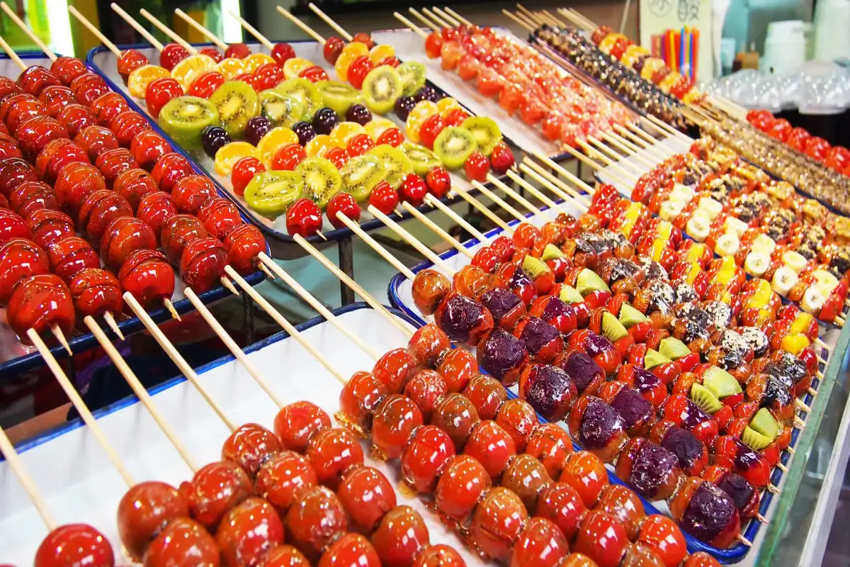 Colorful candied haws skewers with hawthorns, kiwi, tomatoes, and sesame toppings arranged on trays