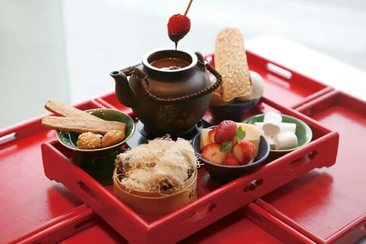Chocolate fondue with dipping items: strawberries, marshmallows, cookies, melon slices and pastries on red tray
