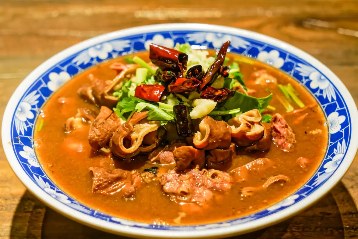 Braised pig intestines in rich brown broth with coriander and red chilies, served in blue-and-white bowl