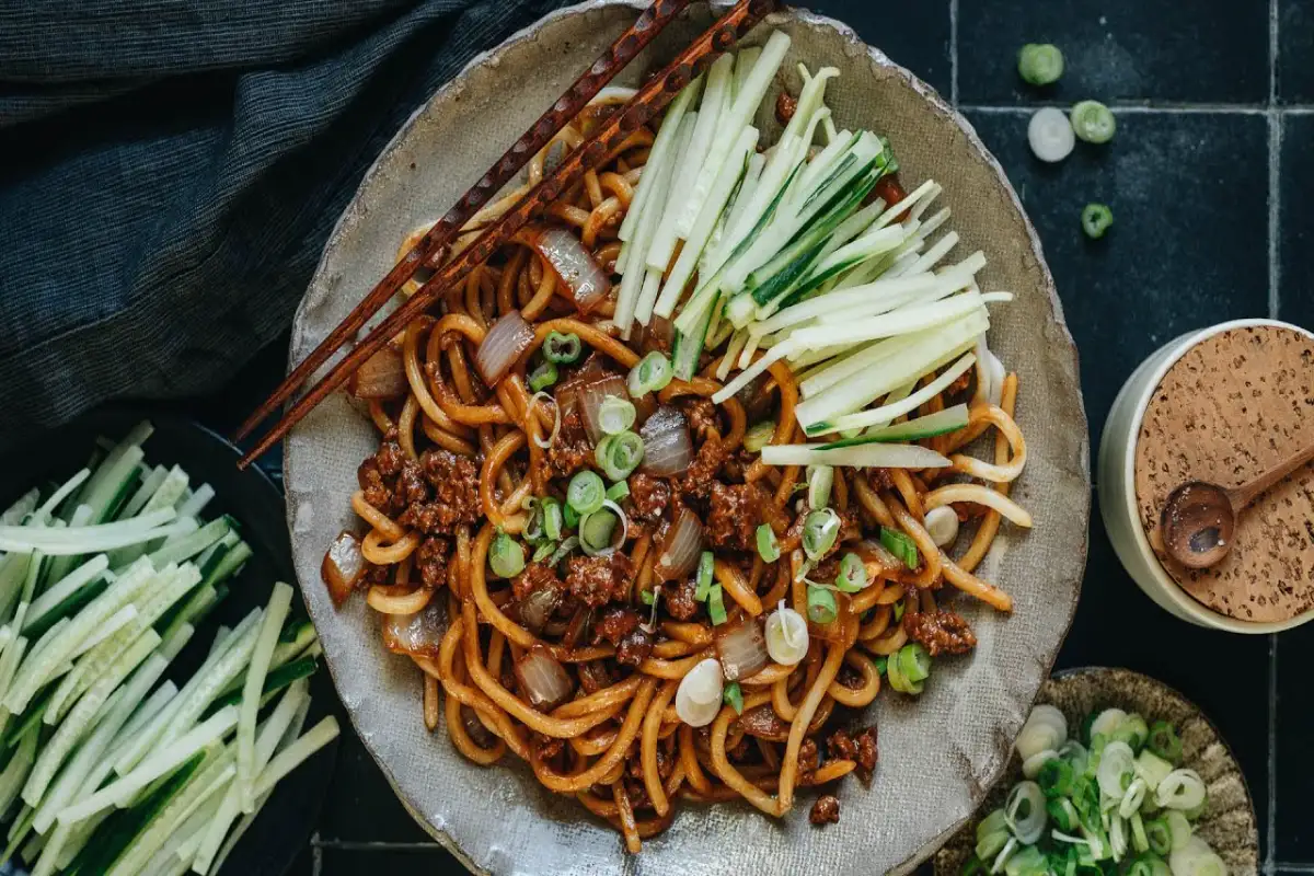 Delicious minced meat noodles with fresh cucumbers, green onions, and brown sauce, served with chopsticks